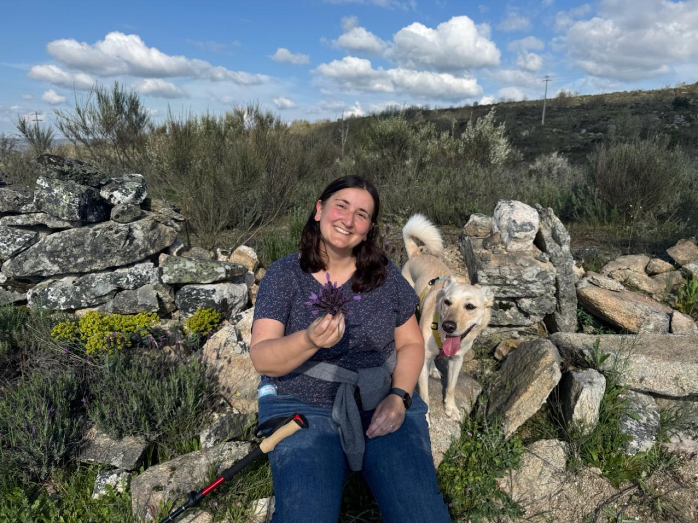 Cristina Budzinski, assise dans la rocaille avec deux chiens, une plante à la main